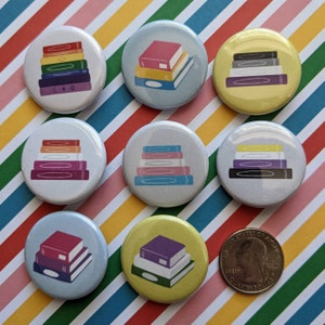 Op de afbeelding: Tien kleurrijke ronde knoppen met stapels boeken erop. De knoppen zijn gerangschikt in twee rijen van vijf. De knoppen zijn allemaal in verschillende kleuren, waaronder rood, oranje, geel, groen, blauw, paars, roze en wit. De boeken op de knoppen zijn allemaal in verschillende kleuren en maten.