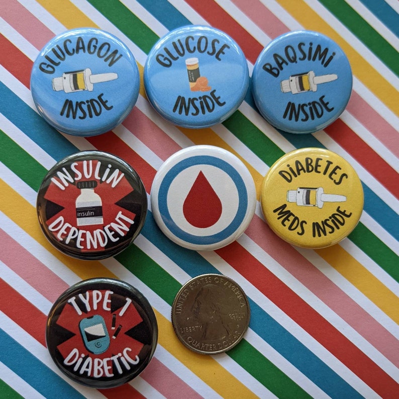 May include: Seven round buttons with various designs related to diabetes. The buttons are blue, yellow, black, and red with white text and images. The text on the buttons includes "Glucagon Inside", "Glucose Inside", "Insulin Dependent", "Diabetes Meds Inside", "Type 1 Diabetic", "Baqsimi Inside", and a red blood drop symbol.