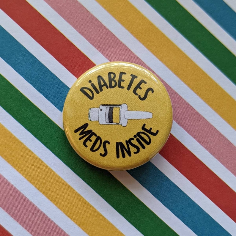 May include: Yellow button with black text that reads "Diabetes Meds Inside". A black and white illustration of a syringe is in the center of the button.