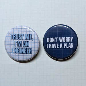 May include: Two round button pins with white text on a blue and white grid background. The first pin says "Trust me, I'm an engineer". The second pin says "Don't worry, I have a plan".