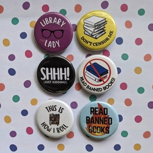 Op de afbeelding: Zes ronde knopen met verschillende ontwerpen met betrekking tot boeken en lezen. De knopen zijn wit, zwart, geel, paars, blauw en rood. De tekst op de knopen is "Library Lady", "Don't Censor Me", "Shhh! (Just Kidding!)", "Read Banned Books", "This is How I Roll" en "Read Banned Books".