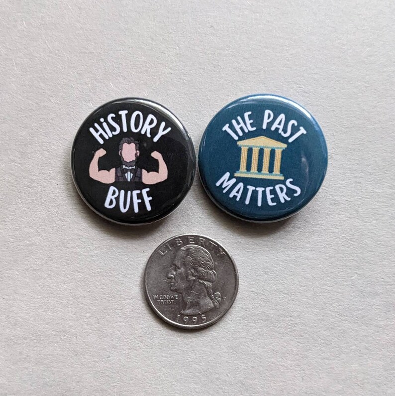 Puede incluir: Dos botones redondos negros y azules con texto blanco. El bot&oacute;n negro dice "History Buff" y presenta una ilustraci&oacute;n de dibujos animados de un hombre con barba flexionando sus b&iacute;ceps. El bot&oacute;n azul dice "The Past Matters" y presenta una ilustraci&oacute;n amarilla de un edificio con columnas.