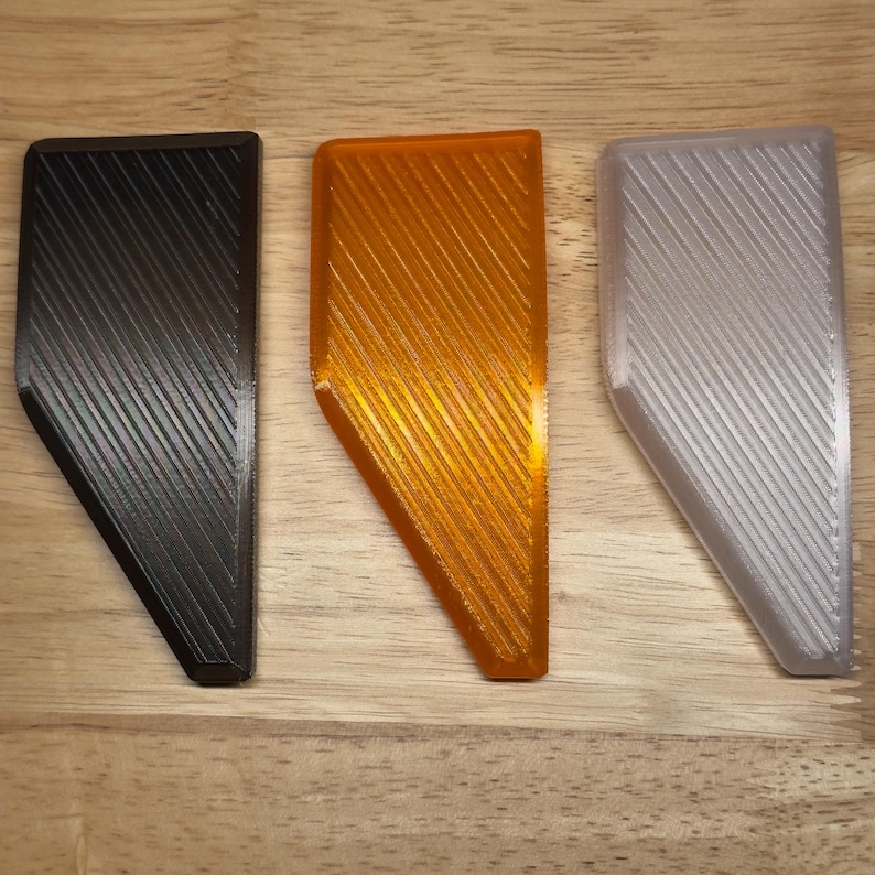 May include: Three plastic triangular shapes with a textured surface. The shapes are black, orange, and white.