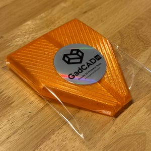 May include: Orange 3D printed object in a clear plastic bag with a silver sticker that says "GadCAD 3D" and "Proudly 3D Printed in Texas" with the website "www.gadcad3d.com".