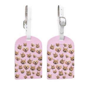 May include: Two pink luggage tags decorated with a repeating pattern of cat and dog faces. Each tag has a white strap and a silver buckle. These travel tags are designed with a fun pet theme.