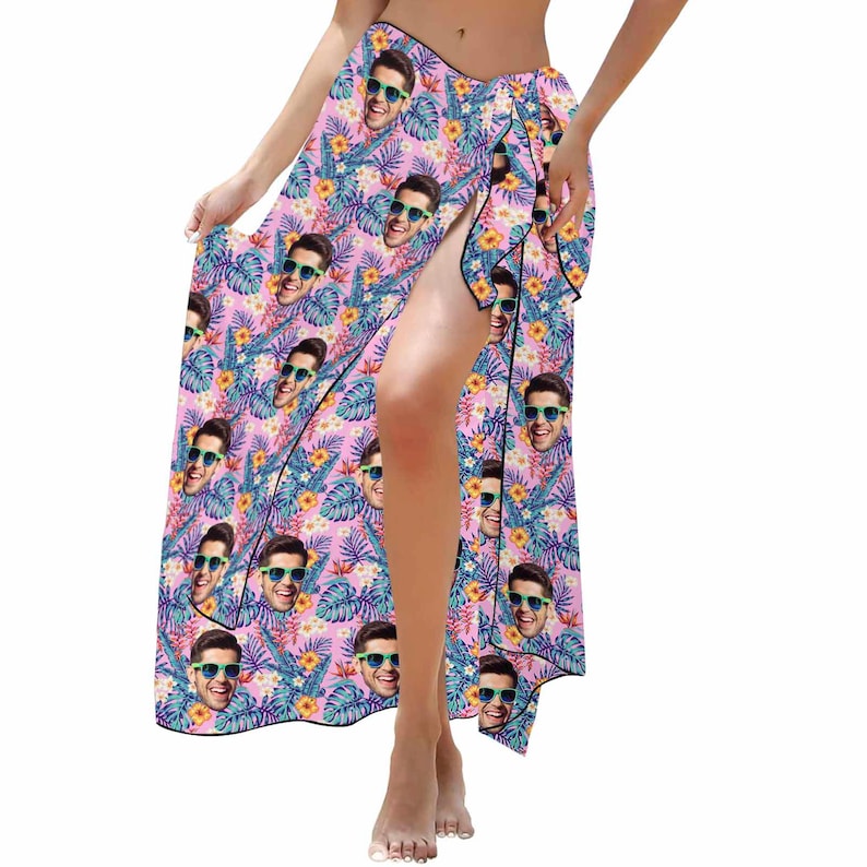 Puede incluir: Un pareo rosa con estampado tropical que presenta un patr&oacute;n repetido de la cara de una persona con gafas de sol. El pareo est&aacute; atado a la cintura y tiene una abertura en el lateral.