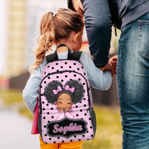 May include: Pink backpack with black polka dots and a cartoon illustration of a girl with curly hair and pink bows. The backpack has the name "Sophia" in a decorative frame.