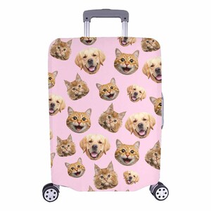 May include: A pink suitcase cover with a repeating pattern of smiling golden retriever and ginger cat faces. The luggage cover has a retractable handle and two wheels.