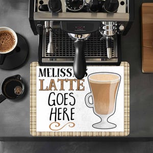 May include: A white kitchen mat with a brown plaid border. The mat has the text "Melissa's Latte Goes Here" in black lettering and a cartoon image of a latte in a glass.