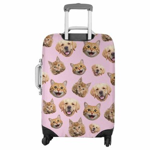 May include: A pink suitcase covered in a pattern of smiling golden retriever and ginger cat faces. The luggage has a retractable handle, a side handle, and black wheels. The case is designed for travel.