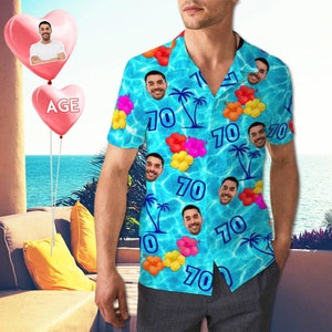 Op de afbeelding: Een blauw en wit Hawaiiaans overhemd met een zwembadpatroon en het getal 70 dat overal wordt herhaald. Het overhemd heeft een kraag en korte mouwen.
