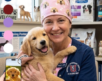 May include: A light pink scrub cap featuring a repeating pattern of golden retriever puppy faces and white paw prints. The cap is worn by a person holding a golden retriever puppy, with a smartphone displaying the same puppy image.
