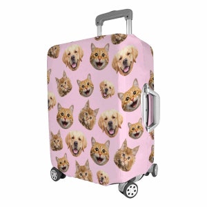 May include: A pink suitcase cover with a repeating pattern of smiling golden retriever and ginger cat faces. The suitcase has a retractable handle and wheels, designed for travel. The cover is made of a durable material.