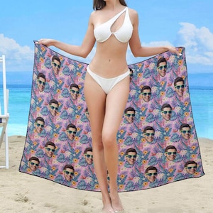 Puede incluir: Una toalla de playa rosa con un patr&oacute;n de hojas tropicales y m&uacute;ltiples caras de personas con gafas de sol. La toalla est&aacute; envuelta alrededor de una persona que lleva un bikini blanco.