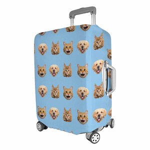 May include: A light blue suitcase cover with a repeating pattern of smiling golden retriever and cat faces. The suitcase has a silver handle and wheels, designed for travel and luggage protection.
