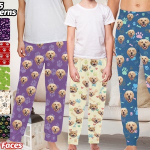 Könnte beinhalten: Ein Set mit drei Pyjama-Hosen mit verschiedenen Hundegesichtern und Pfotenabdrücken. Die Pyjamas sind in Lila, Creme und Blau erhältlich. Der Text "25 Muster" und "1-10 Gesichter" ist auf dem Bild zu sehen.