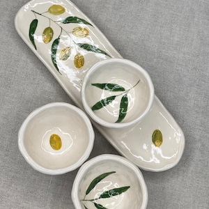 Könnte beinhalten: Eine weiße Keramik-Servierplatte mit drei kleineren Schalen. Die Platte und die Schalen sind mit einem handgemalten Olivenzweig-Design in Grün- und Goldtönen verziert.