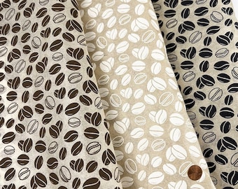 May include: Three sheets of light-colored fabric featuring a repeating coffee bean pattern. The left sheet has dark brown beans, the center sheet has white beans, and the right sheet has black beans. A copper penny rests on the bottom right.