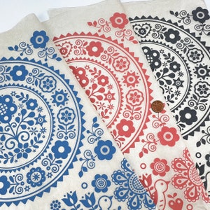 Pode incluir: Três amostras de tecido com fundo branco e um padrão repetitivo de desenhos florais azuis, vermelhos e pretos. Os desenhos são circulares e apresentam flores, folhas e estrelas estilizadas.