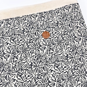 May include: White fabric with a black and white floral pattern. The fabric has a repeating pattern of stylized flowers.