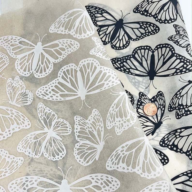 May include: Two sheets of wrapping paper with a butterfly pattern. One sheet has white butterflies on a beige background, and the other sheet has black butterflies on a beige background.