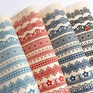 May include: Four rolls of decorative paper featuring lace patterns in red, blue, and black. The paper has a cream background and displays floral and geometric lace designs. The rolls are arranged side by side, showcasing the different patterns.