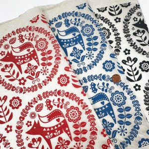 Peut inclure: Trois échantillons de tissu avec un motif d'art populaire scandinave représentant des renards stylisés, des fleurs et des feuilles. Les échantillons sont blancs avec des motifs rouges, bleus et noirs.