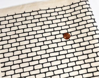 Könnte beinhalten: Ein Stück cremefarbener Stoff mit einem sich wiederholenden schwarzen Ziegelsteinmuster. Eine kupferfarbene Münze liegt auf dem Stoff, um einen Maßstab für die Größe der einzelnen auf das Textilmaterial gedruckten Ziegel zu bieten.