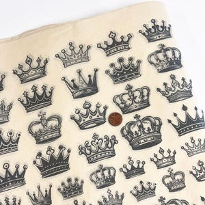 Puede incluir: Una hoja de papel color crema con un patrón repetido de varias ilustraciones de coronas negras. Se incluye una moneda para la escala. Las coronas varían en estilo, con diseños ornamentados y sencillos.