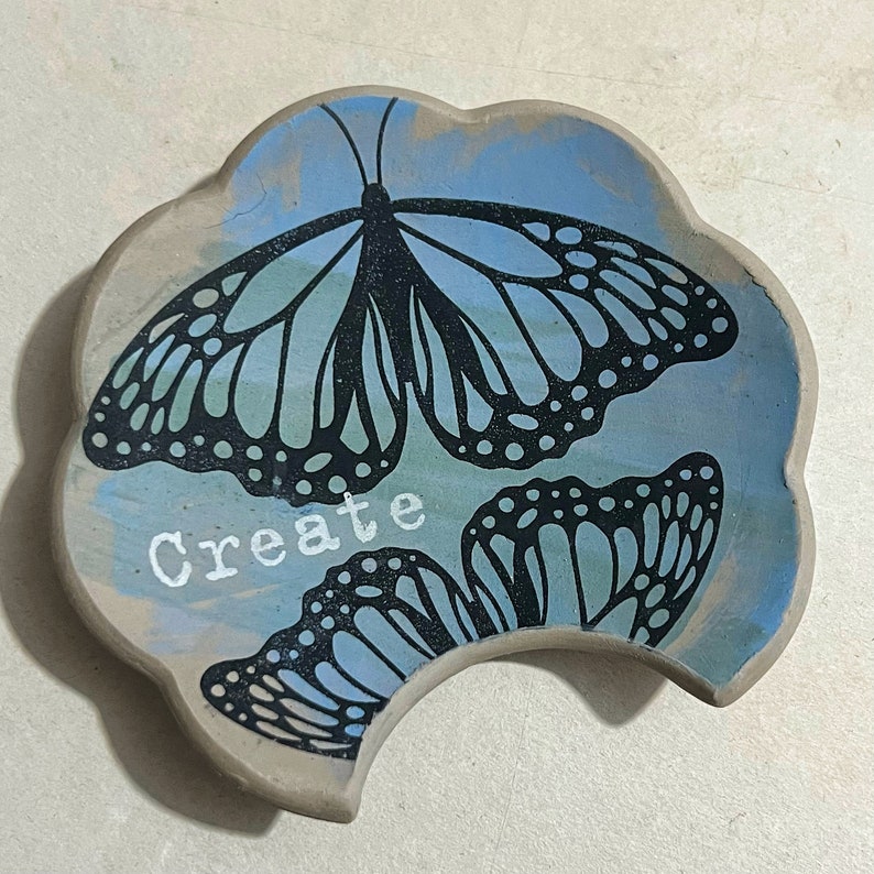 May include: A blue and white ceramic dish with a butterfly design and the word "Create" in white lettering.