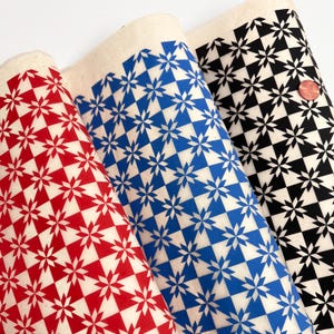 May include: Three rolls of patterned fabric in red, blue, and black. Each roll features a repeating starburst design within a checkered pattern. The fabric has a natural, off-white background, and the designs are in contrasting colors.