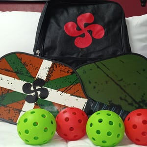 May include: Four green and red pickleball paddles with a black and red backpack. The paddles have a distressed look and feature a green, white, and red design with a black symbol.