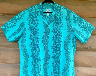 May include: A short-sleeved button-down shirt in a bright turquoise color featuring a dark teal vertical floral pattern of hibiscus flowers and leaves. The shirt has a classic collar, a front button closure, and a single chest pocket on the left side.