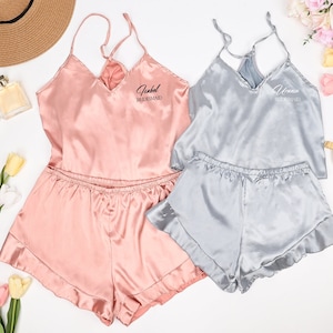 Puede incluir: Dos conjuntos de pijama de satén con ribete de encaje. El conjunto rosa dice "[Name] Dama de honor" y el conjunto gris dice "[Name] Dama de honor".