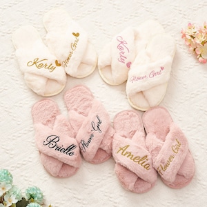 May include: Four pairs of fluffy white and pink slippers with gold lettering. Each slipper has the name "Karly", "Brielle", "Amelia", or "Flower Girl" embroidered on them.