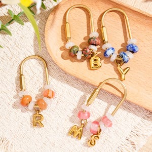May include: Four gold-toned U-shaped metal keychains featuring colorful beads and hanging gold-toned letter charms. The charms spell out the letters B, Y, R, M, and S. Each keychain is adorned with a mix of white, orange, pink, green, and blue beads.
