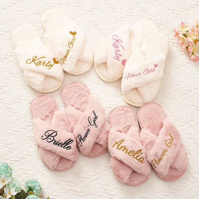 May include: Four pairs of fluffy white and pink slippers with gold lettering. Each slipper has the name "Karly", "Brielle", "Amelia", or "Flower Girl" embroidered on them.
