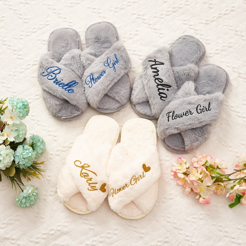 May include: Three pairs of fluffy slippers with embroidered names and the words "Flower Girl". The slippers are in grey and white.