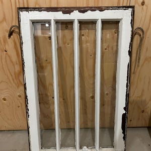 May include: A white painted wooden window frame with four panes of glass. The frame has a dark brown wood trim around the edges and is slightly weathered.