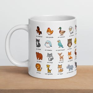 May include: White ceramic mug featuring colorful cartoon illustrations of various animals, each labeled with a French word. The mug includes images of a horse, chicken, duck, sheep, cat, bird, parrot, owl, bear, wolf, deer, fox, lion, giraffe, tiger, and rhino.