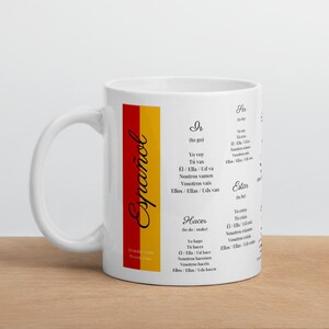 May include: White ceramic mug with a red and yellow Spanish flag design. The mug features a list of Spanish verb conjugations for the verbs "ir" (to go), "hacer" (to do), and "estar" (to be).