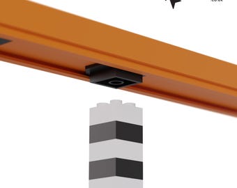 May include: A black plastic connector piece for a Lego-compatible track system. The connector is attached to a white and black Lego-compatible brick.