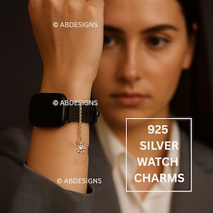 Może przedstawiać: Czarny smartwatch ze złotym łańcuszkiem z małym, białym kwiatowym wzorem z przezroczystym kamieniem centralnym. Tekst "925 SILVER WATCH CHARMS" jest wyświetlany w białym polu.