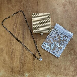May include: A black beaded necklace with a silver pendant, a small woven box, and a white lace bag.
