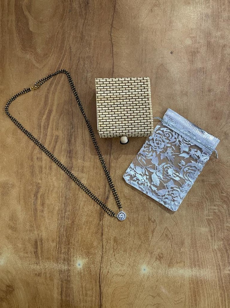 May include: A black beaded necklace with a silver pendant, a small woven box, and a white lace bag.