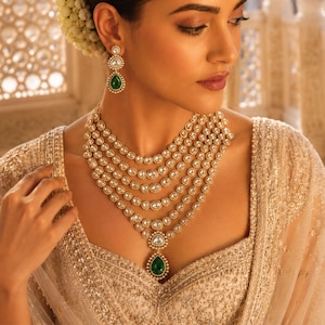Peut inclure: Un collier doré à plusieurs rangs composé de cinq chaînes de pierres rondes transparentes et d'un pendentif central en forme de goutte vert. Des boucles d'oreilles assorties en forme de goutte verte avec des pierres transparentes.