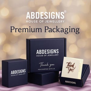 Może przedstawiać: Granatowe pudełka na biżuterię z napisem "ABDESIGNS HOUSE OF JEWELLERY" i "Premium Packaging". Jedno pudełko jest otwarte, ukazując kartkę z napisem "Thank You!" złotym pismem. Pudełka są ułożone na rozmytym tle.