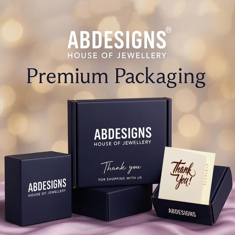 Może przedstawiać: Granatowe pudełka na biżuterię z napisem "ABDESIGNS HOUSE OF JEWELLERY" i "Premium Packaging". Jedno pudełko jest otwarte, ukazując kartkę z napisem "Thank You!" złotym pismem. Pudełka są ułożone na rozmytym tle.