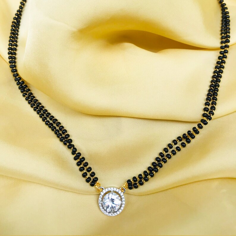 May include: A black beaded necklace with a gold pendant featuring a large, clear, round gemstone.