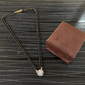 May include: A black beaded necklace with a gold pendant featuring a large, clear, round stone surrounded by smaller stones.